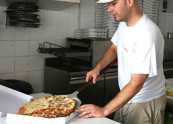 Worker slides pizza into a box